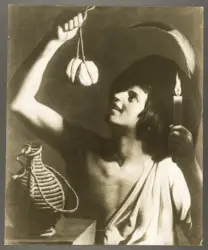 Giovane uomo con in mano una candela accesa che solleva un formaggio e un fiasco posato di lato